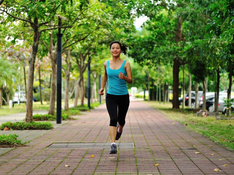 A woman jogs along a brick pathway wearing a teal tank top and leggings.  She uses the Phonak Stick 'n' Stay Hearing Aid Stickers (30 pair) 098-0353 Adhesives so that her hearing aid and Cochlear implant do not fall off and get lost while she is running.