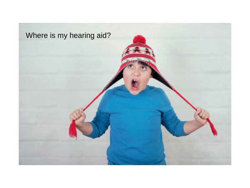 Where is my hearing aid? Use the Phonak Stick 'n' Stay Hearing Aid Stickers (30 pair. This boy in a long sleeved blue t-shirt is holding his red winter hat or toque by the tie strings as he looks up at the ceiling with his mouth open in frustration.