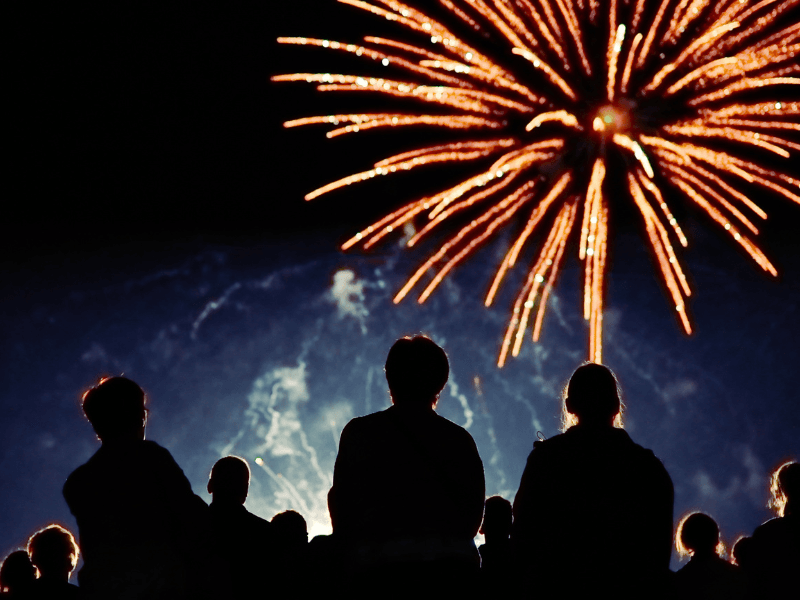Serenity Choice Reusable Hearing Protection used during a fireworks display.  A group of people gather below a red fireworks display. 