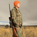 Serenity Choice Reusable Hearing Protection for HUNTING & SHOOTING Earplugs being used by a young woman dressed in an orange tuque and camouflage pants and jacket holding her rifle over her shoulder.  