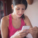 A young woman wearing hearing aids and  in a pink tank top sits on her cell phone.  She uses the Phonak Stick 'n' Stay Hearing Aid Stickers (30 pair) 098-035 Adhesives. 