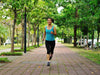 Woman running on a paved path in a park with trees and cars in the background