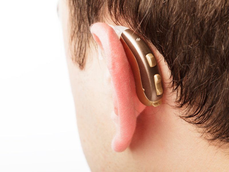 Close-up of a person wearing a gold hearing aid.
