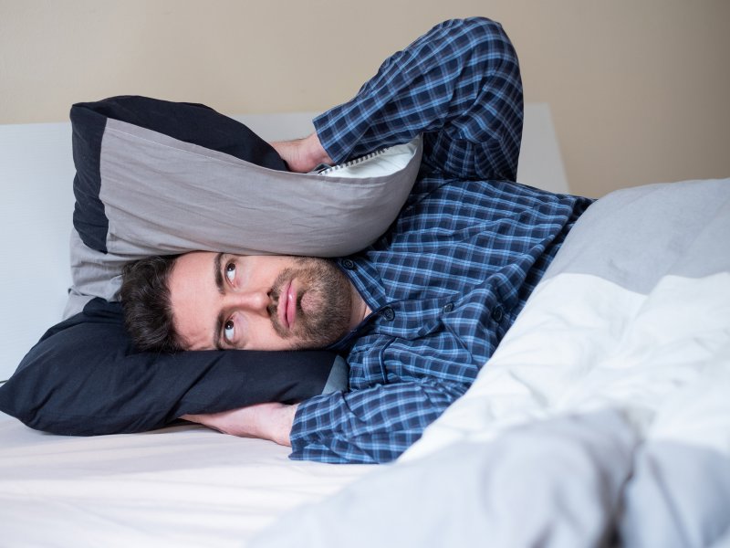 A man lying on a bed with a pillow over his ears, looking confused and tired. tired.