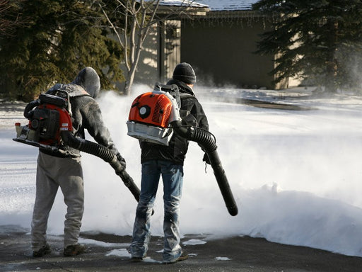 Two people using backpack leaf blowers to clear snow.