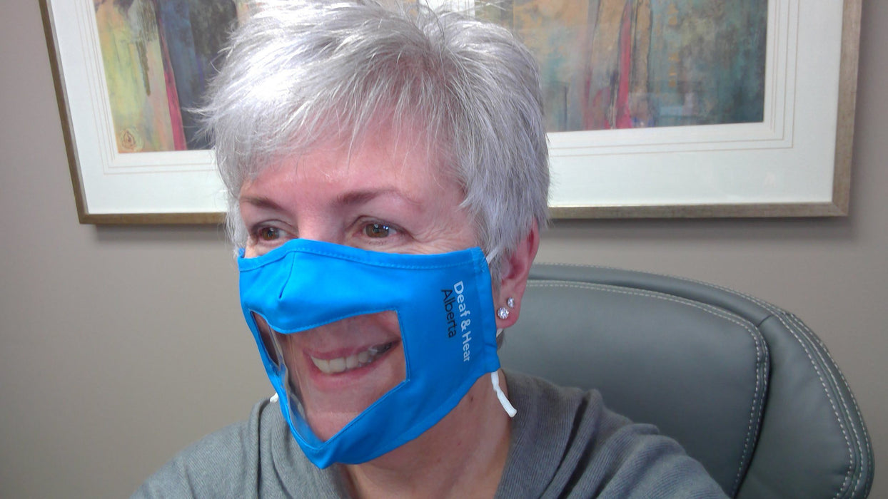 Woman wearing the Blue Fabric Mask with Clear Window and Drawstring Ear Loops Mask.  The mouth and lips are visible through a clear window.  