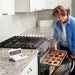 Phot of a woman removing burnt cookie from the oven and the main receiver screen displays the word SMOKE.  Sonic Alert HomeAware Smoke & CO Sound Signaler HA360SSSCK2-1 