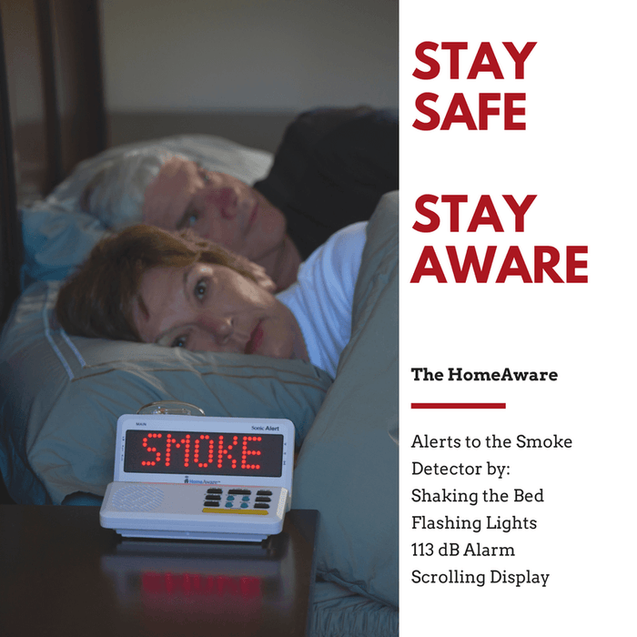 A man and woman lay in bed while the Main Unit of the HomeAware system displays the red word SMOKE.  The Sonic Alert HomeAware Smoke & CO Sound Signaler HA360SSSCK2-1 transmitter has notified them of an emergency alert. 
