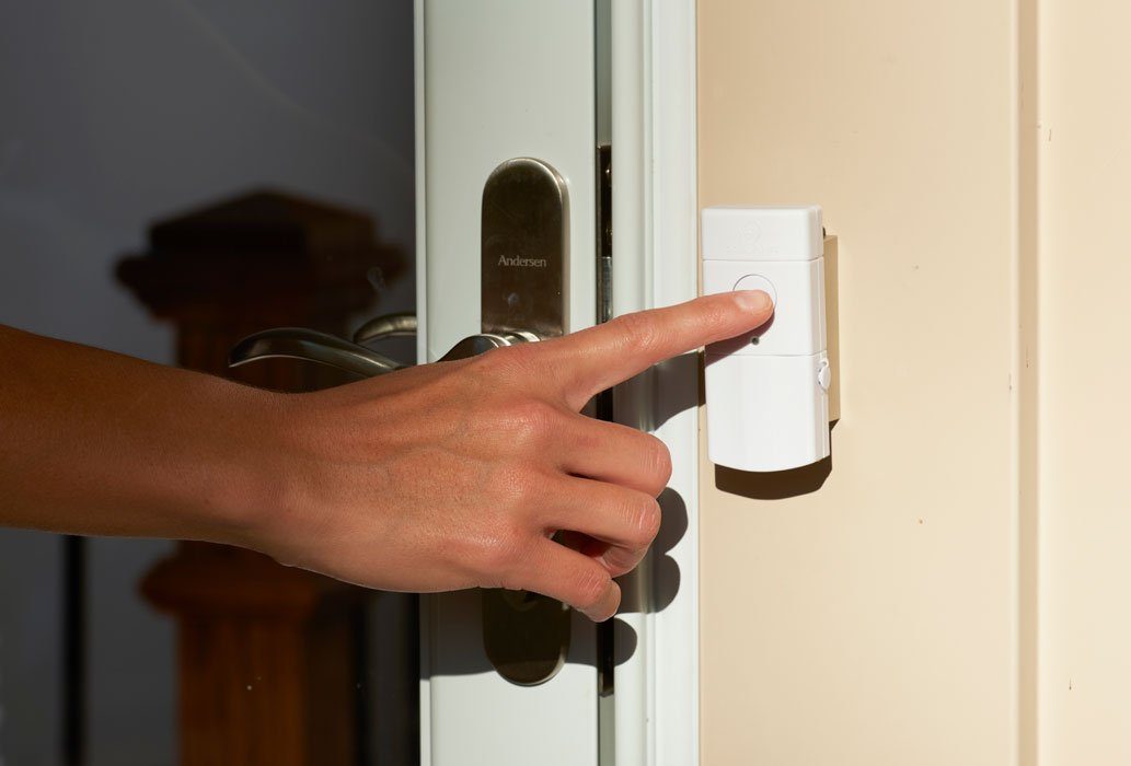 A hand reaches across the door handle to push the button on the Sonic Alert HomeAware™ Wireless Doorbell HA360DB2-1.  