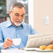 Man reading newspaper and drinking tea with the flashing Wireless Doorbell behind him. 